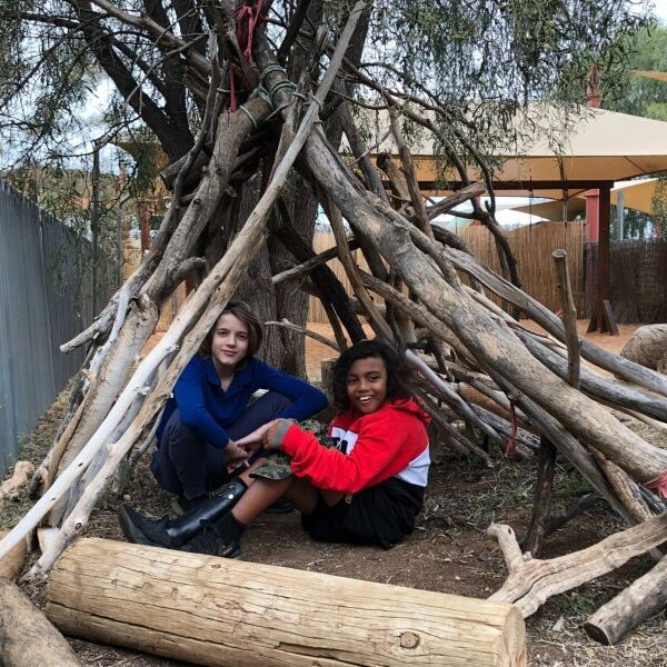 Two teens sitting outside under terr branches smiling